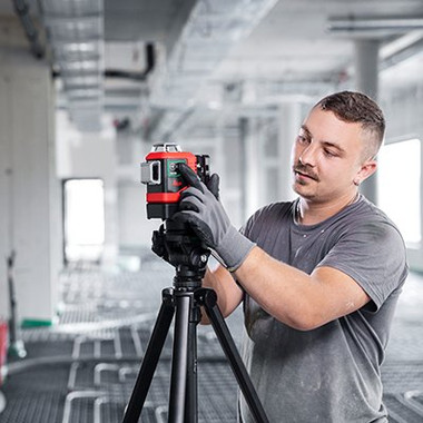 Contractor adjusting a Leica Lino L6G on a tripod on a building site with green laser lines on the walls