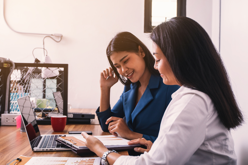 Two women reviewing documents together beside a laptop
