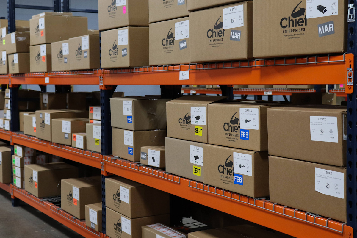 Chief Enterprises warehouse displaying organized shelving with branded brown shipping boxes, highlighting product sourcing and distribution services for OEM and electro-mechanical components