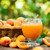 A glass of Apricot Peach juice on a table among scattered apricots.