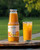 A bottle of Smart Juice organic Apricot Peach juice and in a glass with ice, on a table in a park.