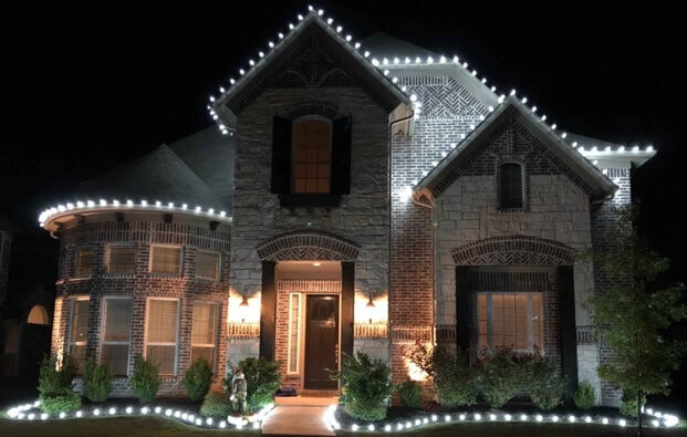A large, two-story house decorated with warm white Christmas lights at night.