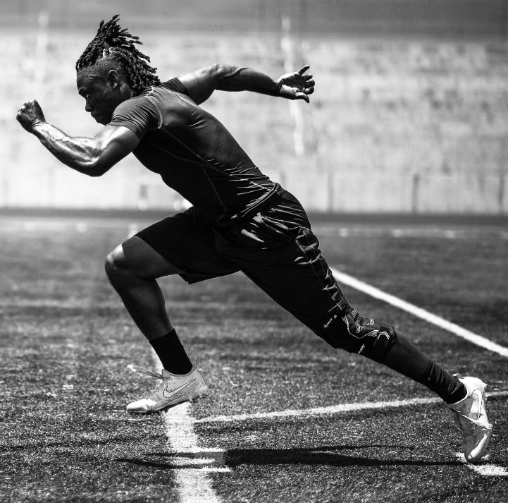 Black-and-white photo of an athlete sprinting on a field while wearing a knee brace.