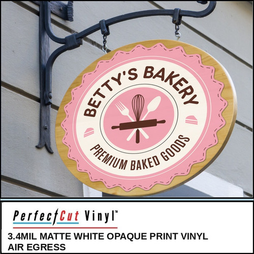 PerfectCut Vinyl 3.4mil matte white opaque print vinyl with air-egress adhesive, shown applied to a round hanging "Betty's Bakery Premium Baked Goods" sign with a pink badge logo and baking utensils.