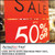 PerfectCut Vinyl 6.0mil matte white semi-rigid print vinyl with removable adhesive, shown as bold red "Sale – Up To 50% Off" retail window graphics on a storefront display.