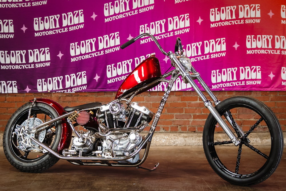 Custom motorcycle with chrome detailing and a red gas tank against a colorful backdrop.