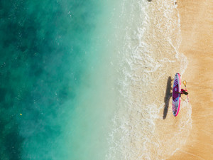 Aerial View of a Surfer Beside a Sapphire Blue Sea