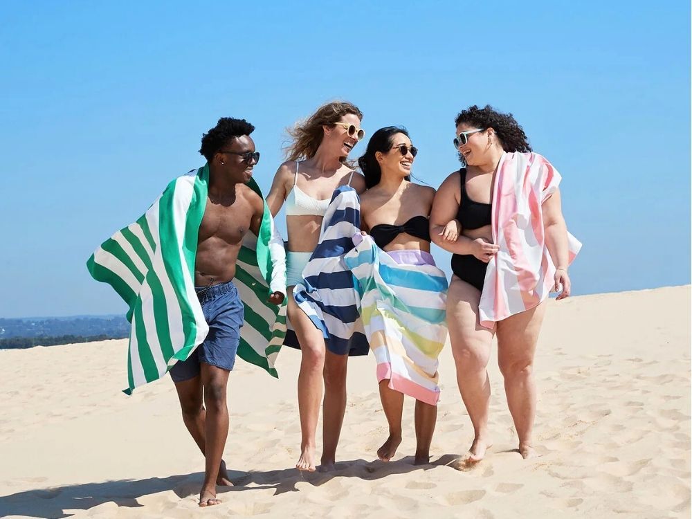 A group of people walking on a beach with Dock & Bay towels