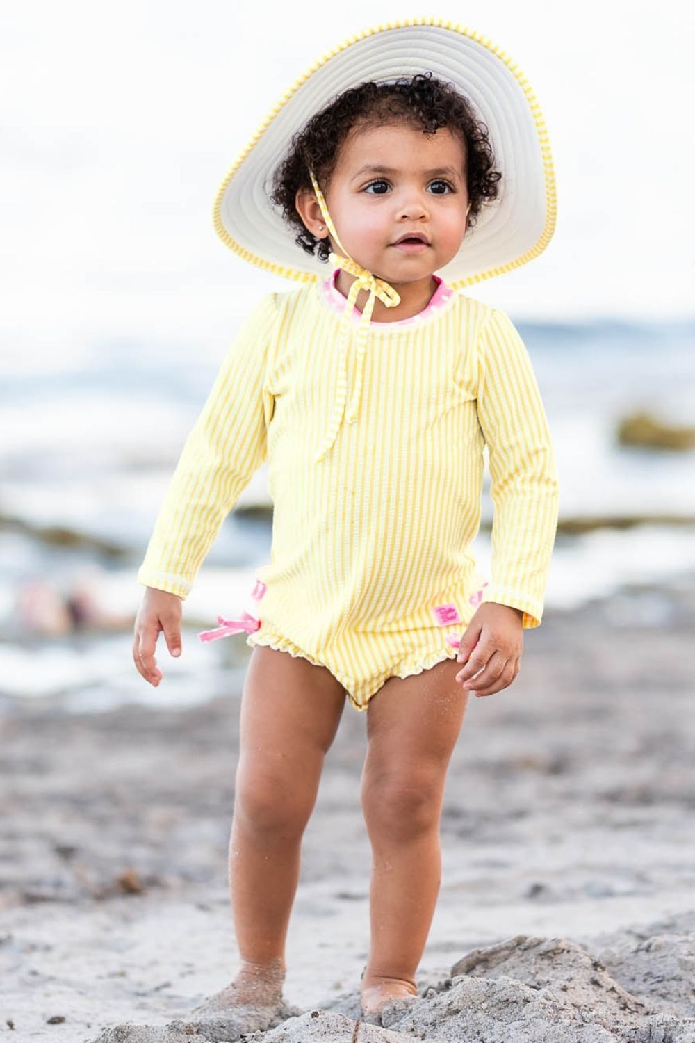 Girl on beach in Yellow Ruffle Butts swimwear