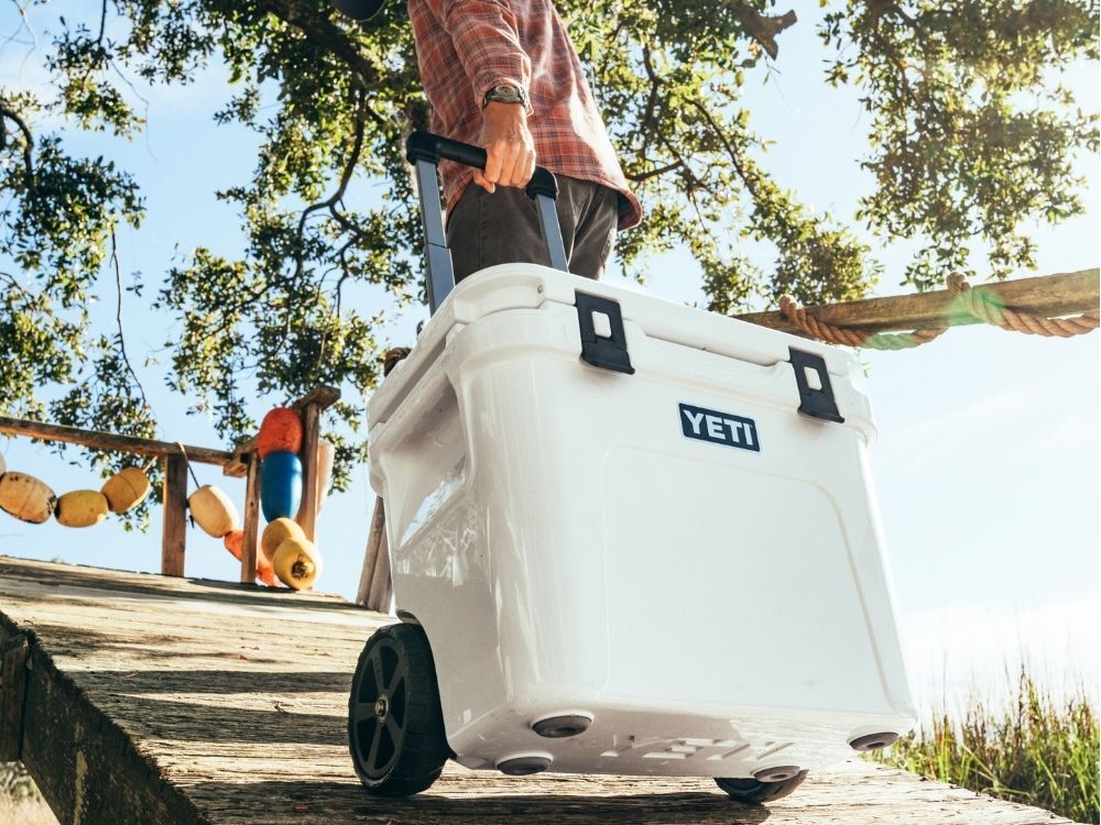 A man rolling a Yeti Wheeled Hard Cooler up a ramp on the beach