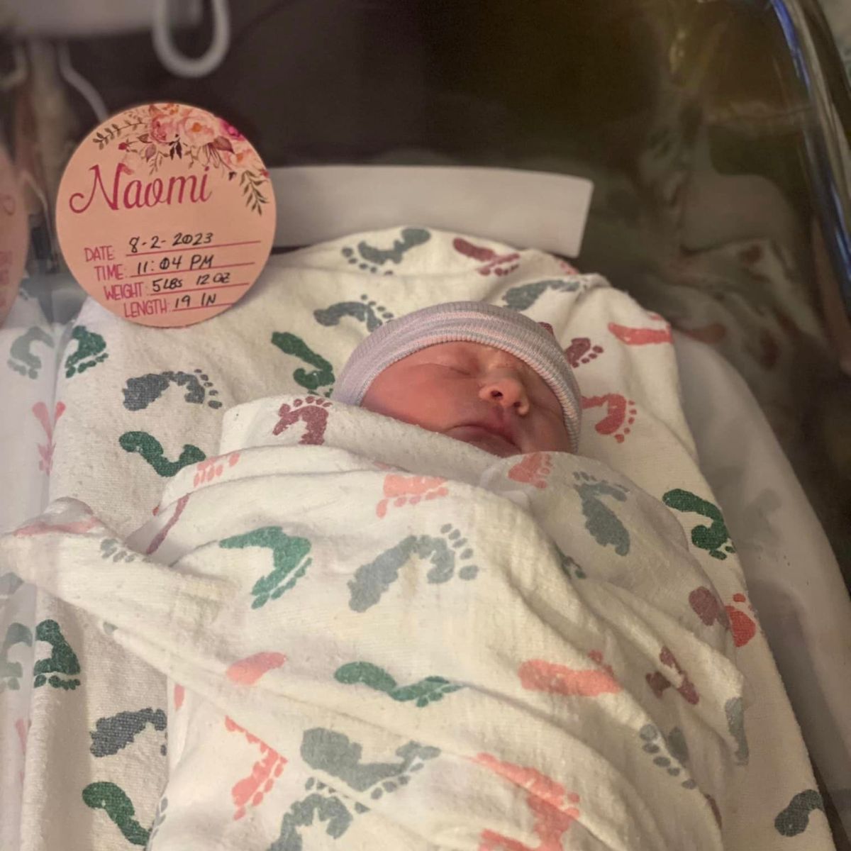 A photo of a baby in a cradle with a sign that reads, "Naomi"