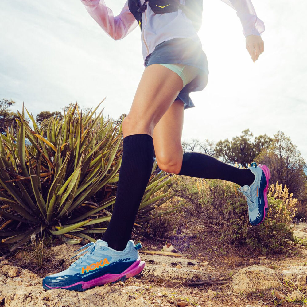 Woman running on a trail wearing HOKA shoes