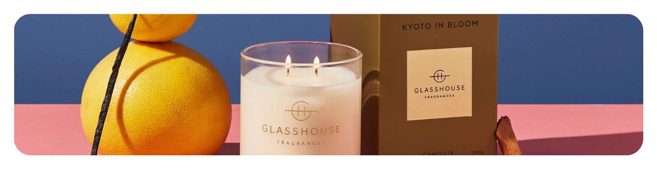 Glasshouse Fragrances lit candle side by side with a box of the scent Kyoto in Bloom and two oranges