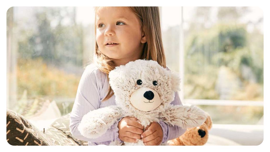 Girl holding stuffed animal teddy bear from brand Warmies