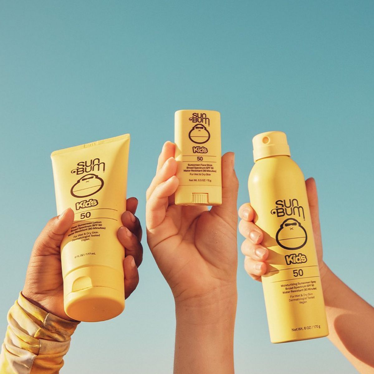 Picture of three children's hands holding Sun Bum kids sun screen products with 50 SPF.