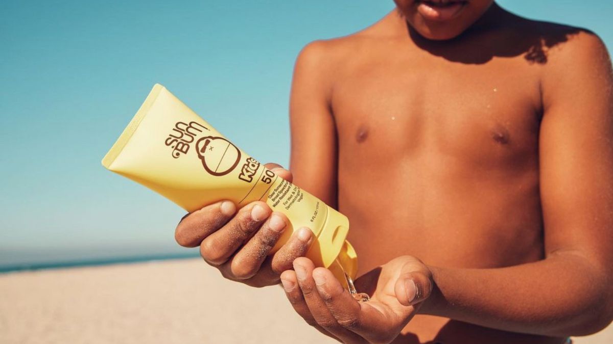 Boy on the beach squeezing some Sun Bum kids 50 SPF sun screen on his hands.