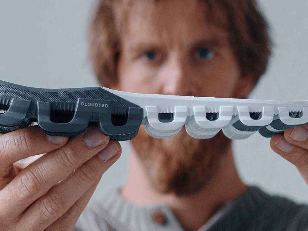 Close up image of man holding the bottom of an On shoe showing CloudTec and his face out of focus in the background.