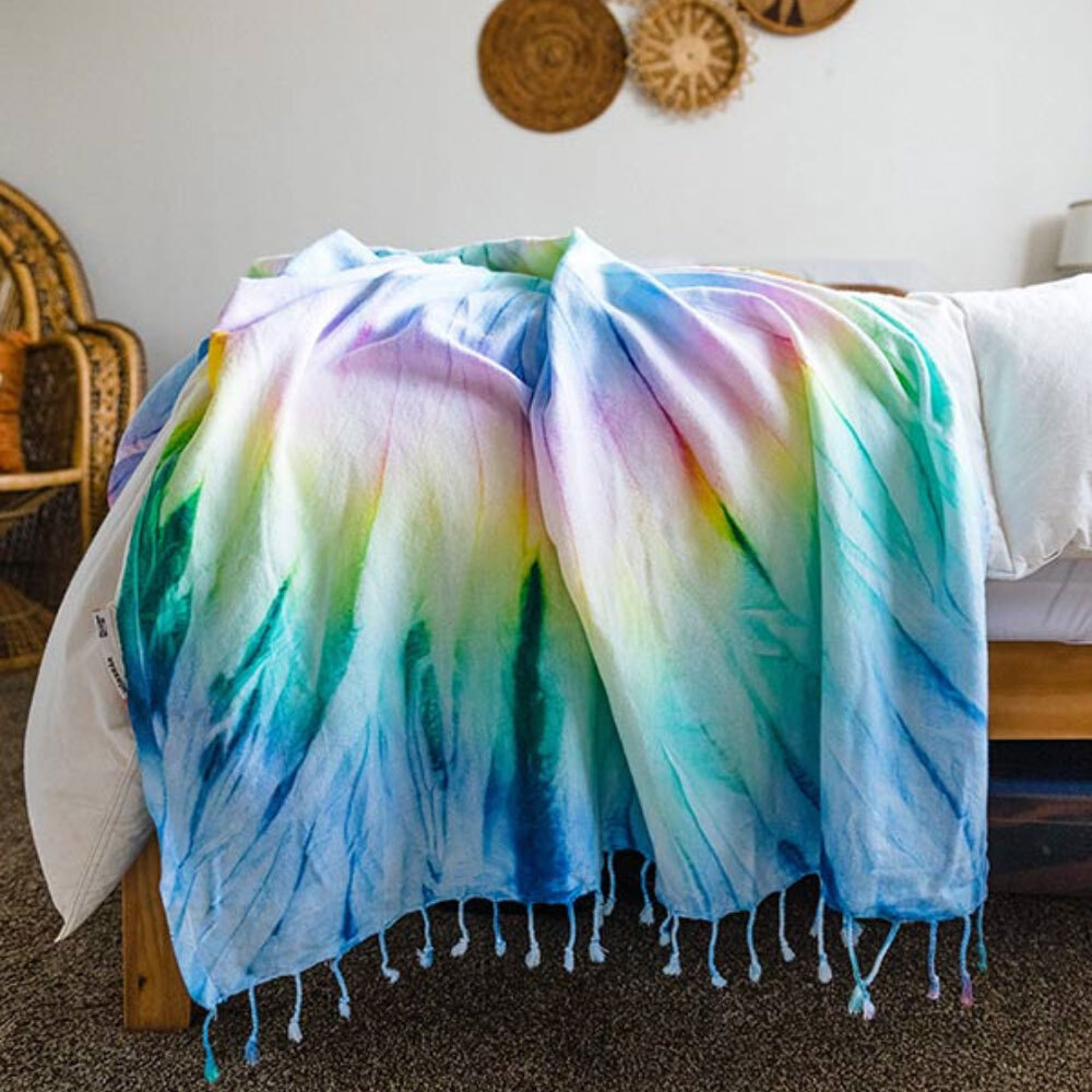 A Sand Cloud tie-dye blanket draped over a bed