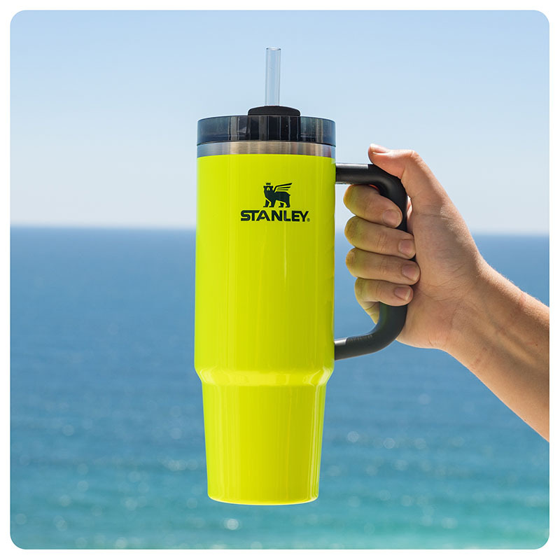 A woman holding a neon yellow Stanley tumbler at the beach