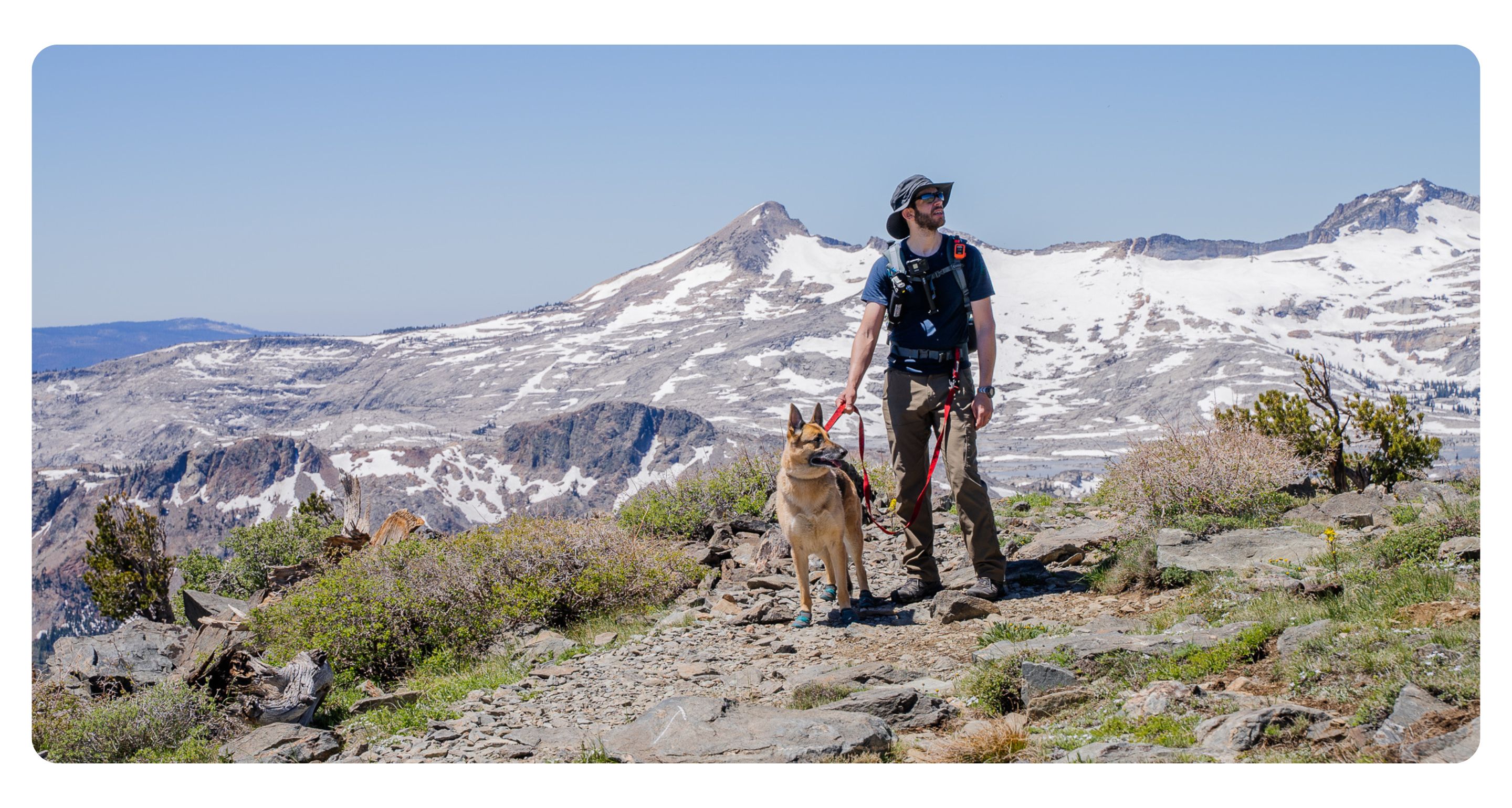 Man hiking with a dog on a snow tipped mountain scene.
