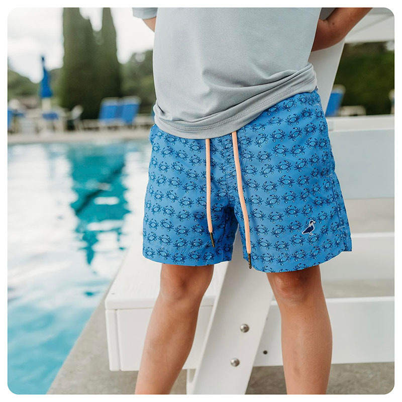 A boy standing poolside wearing Properly Tied swim trunks