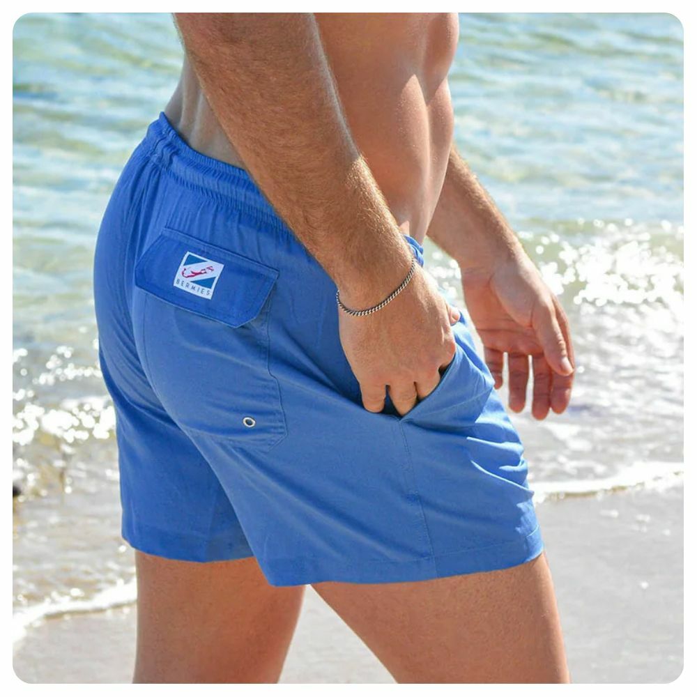 Man walking on a beach wearing blue Bermies swim trunks