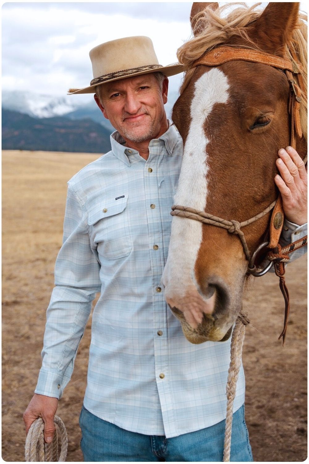 Man wearing flannel button down with his arm around a horse.