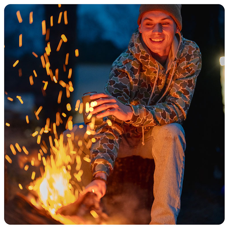 Man sitting in front of fire in Local Boy Outfitters apparel.