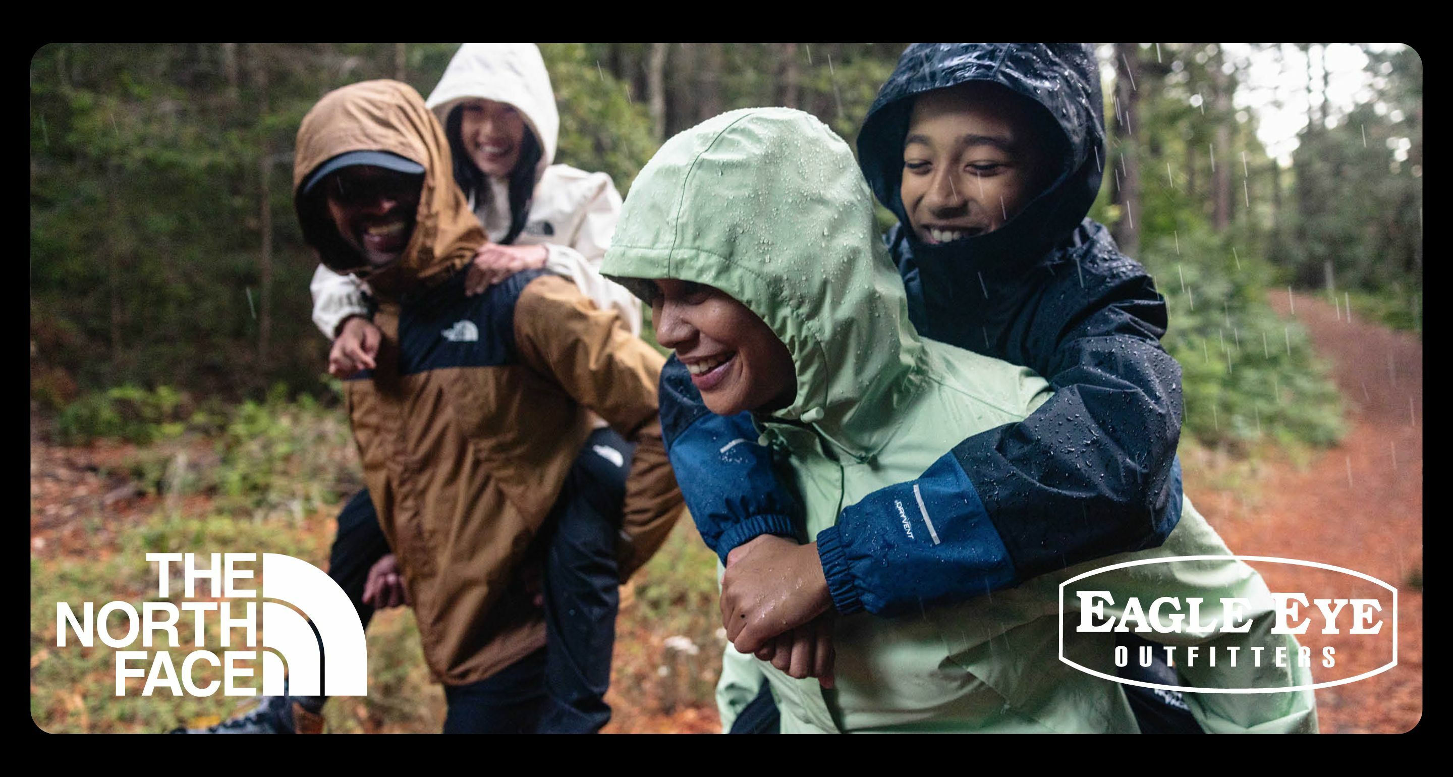 Family all holding hands walking in a Christmas tree farm. They are all smiling and wearing The North Face apparel