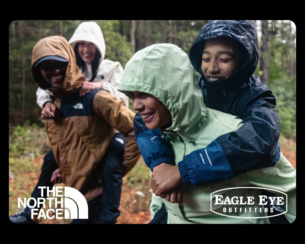 Family all holding hands walking in a Christmas tree farm. They are all smiling and wearing The North Face apparel