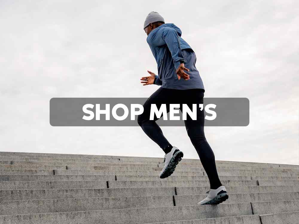 Shop Men's On Shoes at Eagle Eye Outfitters. Man running up steps wearing On shoes, black tights, blue active jacket and grey beanie hat.