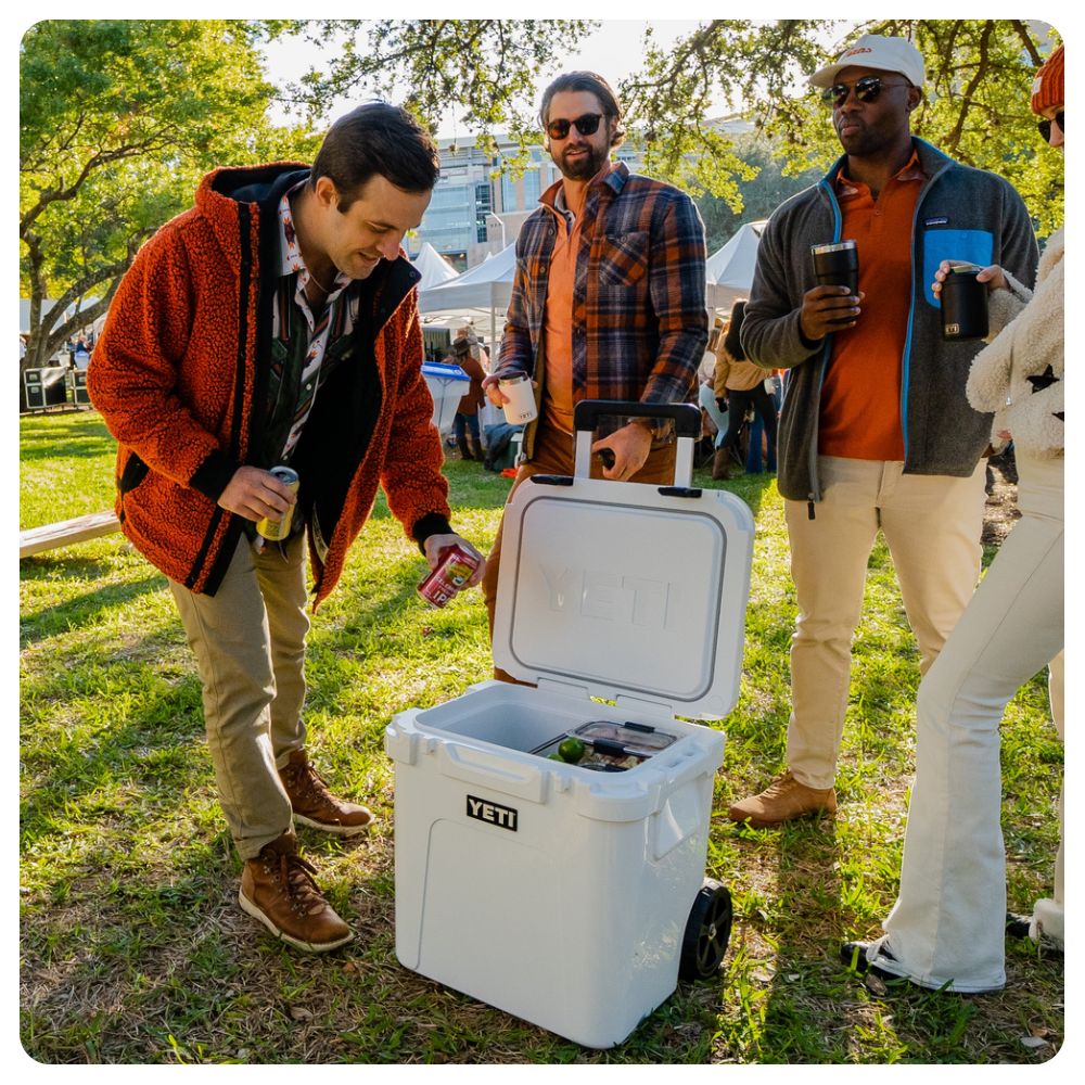 Men and women tailgating around a Yeti Roadie 48 Wheeled Cooler