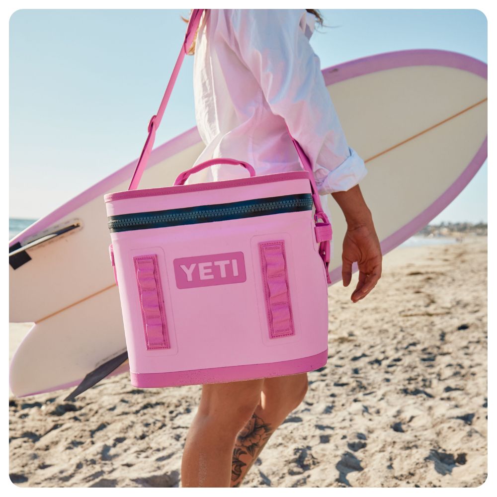 Surfer holding a surf board and Yeti Power Pink Camino Flip Cooler