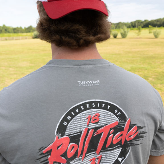 Shop Collegiate Men’s. Back of man wearing University of Alabama red baseball hat and grey Roll Tide t-shirt.