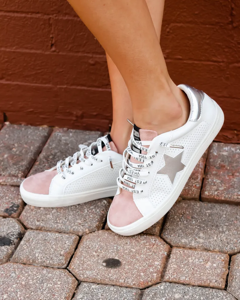 Close-up of a girl on a brick walkway wearing pink, white, and silver Vintage Havana star fashion sneakers.