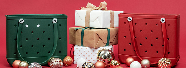 Picture of a hunter green and burgundy Baby Bogg Bags in front of a red background with wrapped presents and ornaments around them.