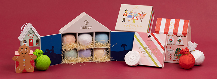 A display of Musee bath bomb gift boxes in front of a red background.