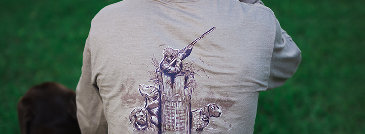 Back of a man wearing a grey long sleeve Over Under t-shirt with a hunting and dog scene on the back.