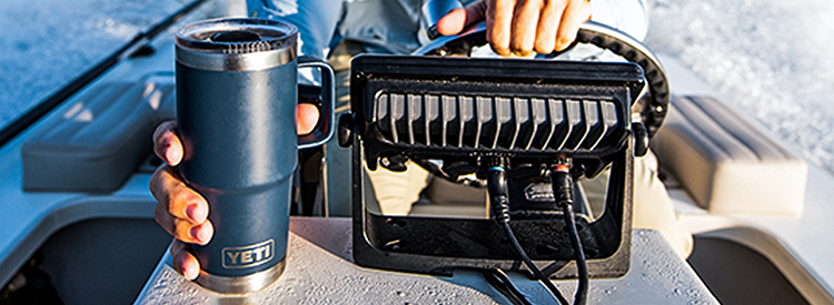 Picture of a man driving a boat steering and holding a navy tall Yeti insulated travel mug.