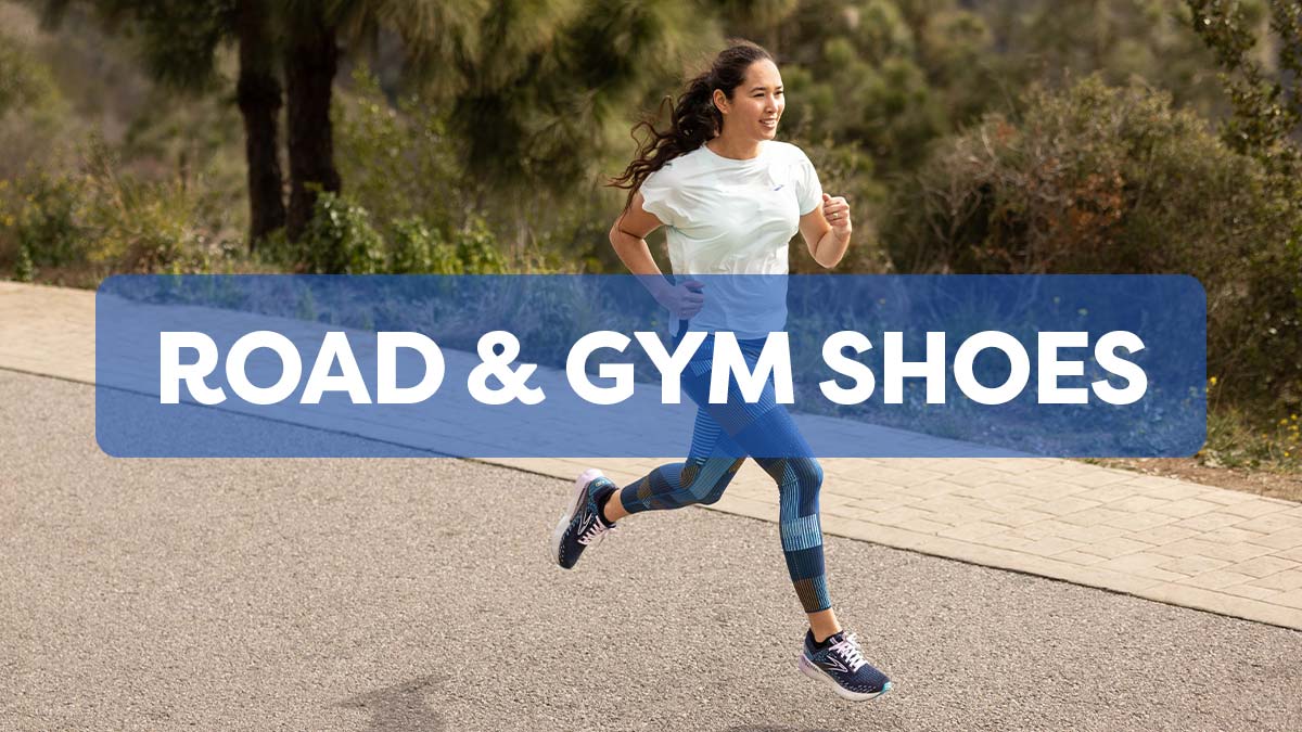 Road & Gym Shoes. Woman running on a paved path wearing blue Brooks Running shoes, blue tights and white active top.