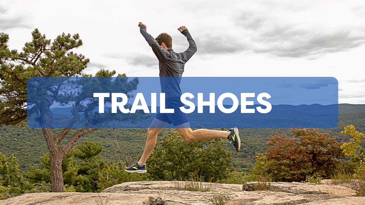 Man leaping on a mountain trail wearing Brooks shoes, shorts and long sleeve performance top.