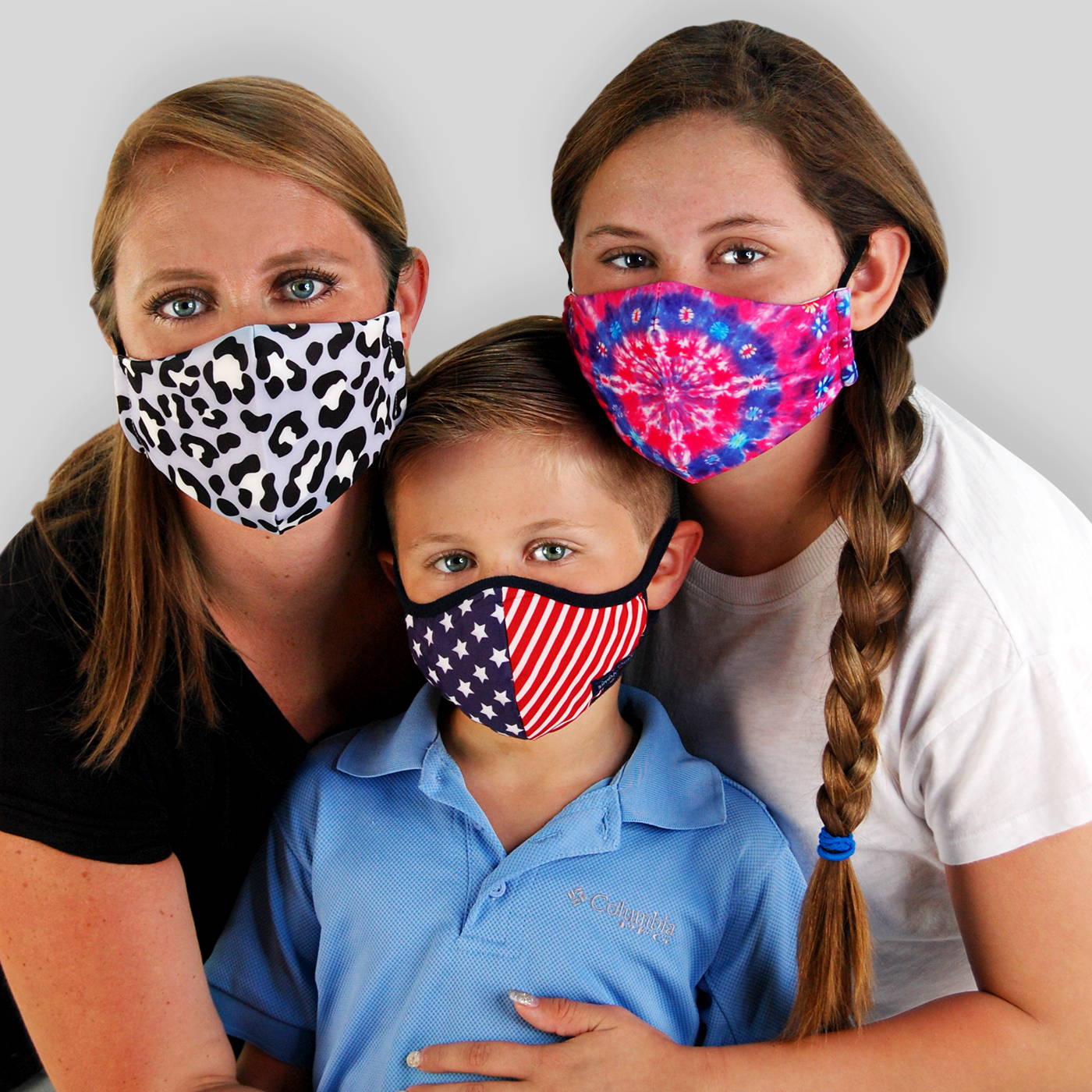 A women with her daughter and son wearing three different face masks. One face mask with a purple leopard print. One with a red, white, and blue stars and stripe print. And one with a multi color blue, purple and pink tie-dye print.