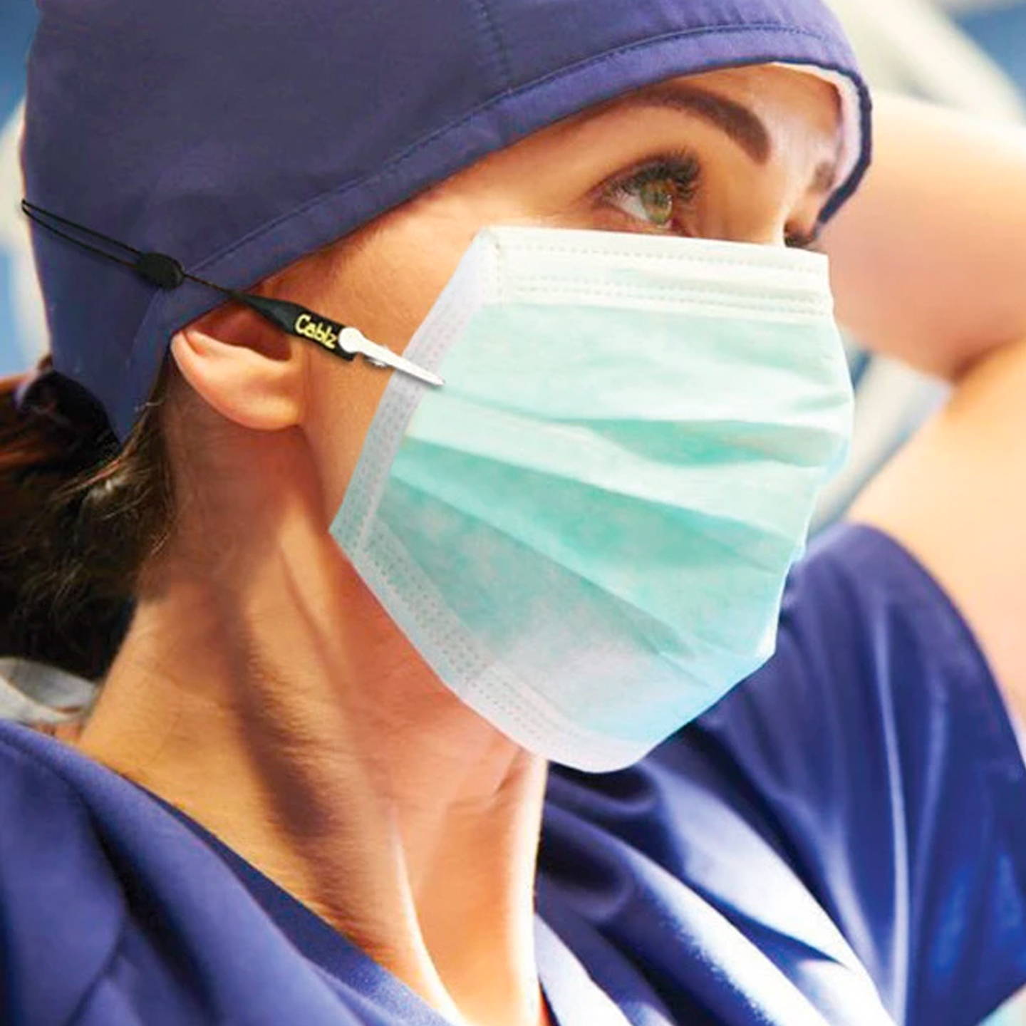 Close up of a nurse in blue scrubs wearing a face mask with a Cablz mask retainer.