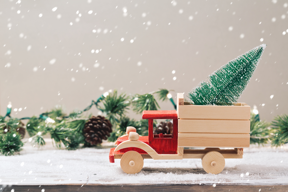 A wooden toy truck carrying a mini Christmas tree in the back, decorated for the holiday season.