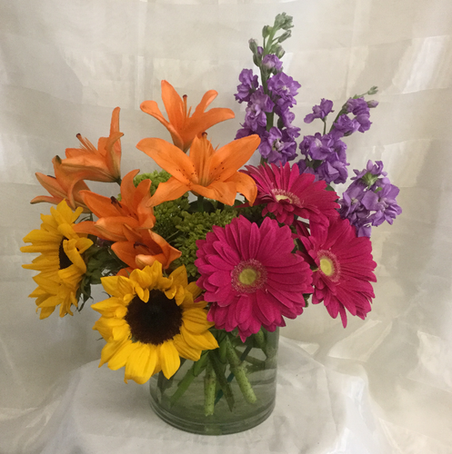 Brighten Her Day Mom's Bouquet by Enchanted Florist Pasadena TX. A bright and lovely bouquet for any mom to enjoy. It includes orange lilies, purple stock, pink gerberas, sunflowers and green hydrangeas designed in a clear cylinder vase.
RM809