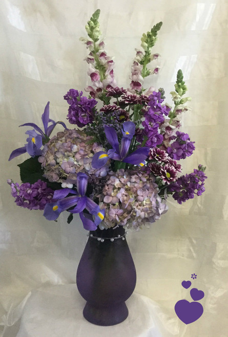 Purple Rain Mothers Day Flowers by Enchanted Florist Pasadena TX is a stunning purple bouquet of iris, hydrangeas, snapdragons and stock in our exclusive pearl wrapped violet frost vase. This all purple bouquet of flowers will tickle any purple lover's fancy and delight your mom on her special Mother's Day. RM804