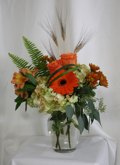 Autumn Dew Drops Bouquet in Orange from Enchanted Florist. Your beautiful fall bouquet will arrive in a clear vase and includes hydrangeas, orange roses, orange gerbera daisies, alstromeria and butterscotch daisies and is accented with sword fern and wheat grass. Approximately 13"W x 17"H
SKU RM212