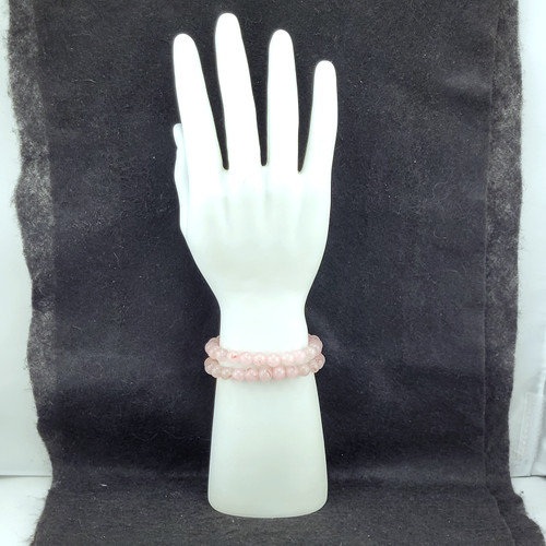Polished pink Rose Quartz bead bracelets stacked on a white mannequin hand display against a dark background.