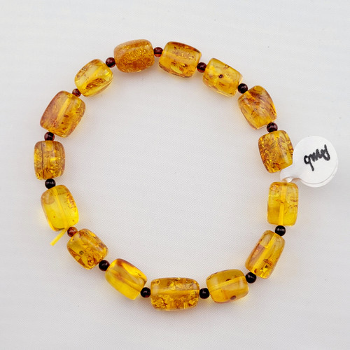 A single strand Flower Amber barrel bead bracelet with small dark accent beads laid flat on a white surface.