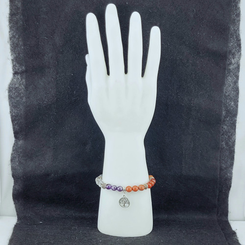 Seven Chakra gemstone bracelet featuring Clear Quartz, Amethyst, and Red Jasper beads with a silver Tree of Life charm on a white mannequin hand.